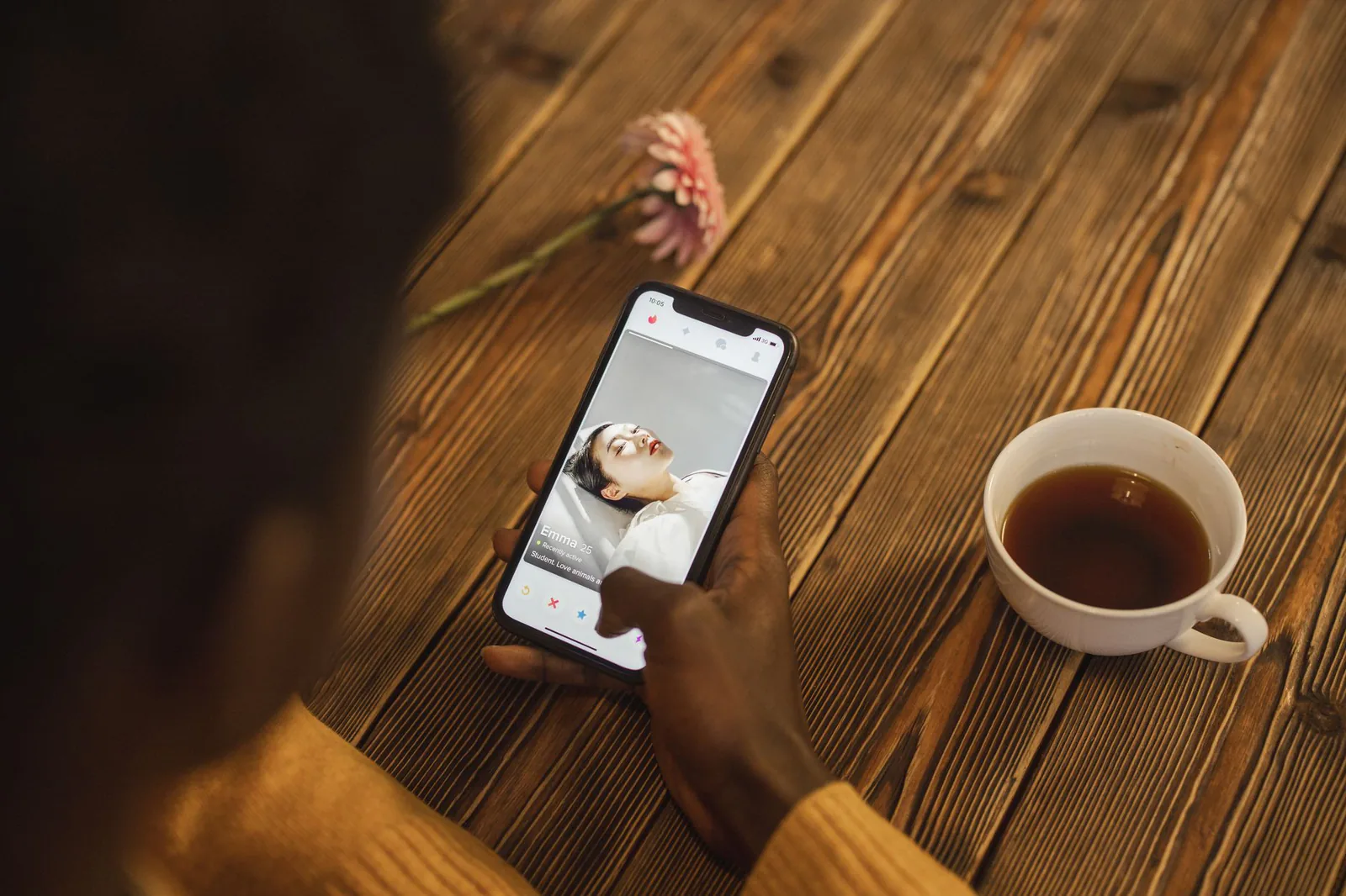 A person using a dating app on a smartphone at a wooden table